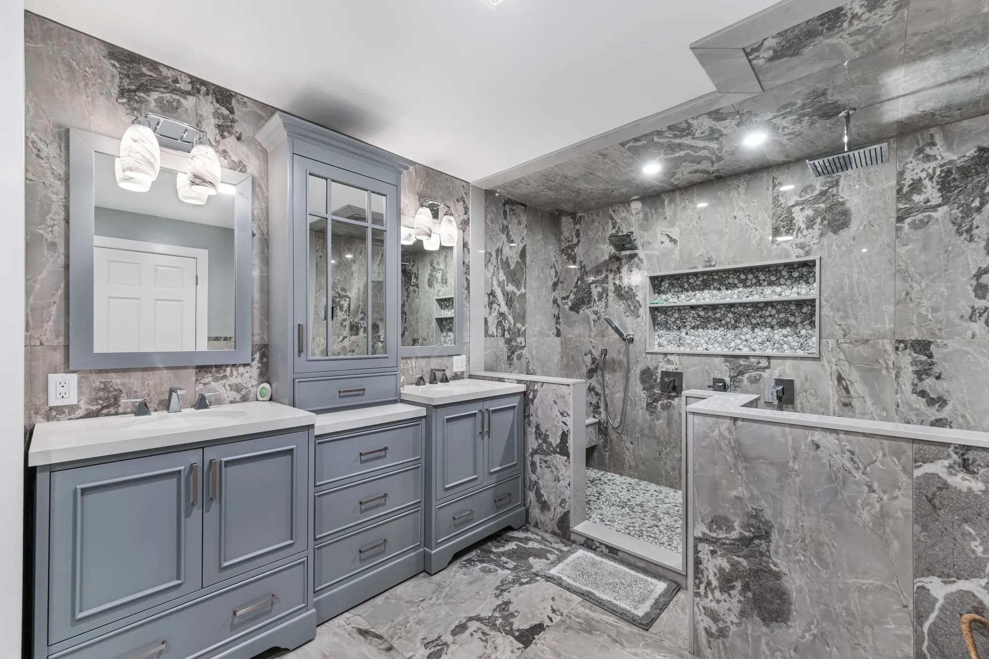 Bathroom with gray cabinetry, double sinks, and a walk-in shower clad in veined gray marble