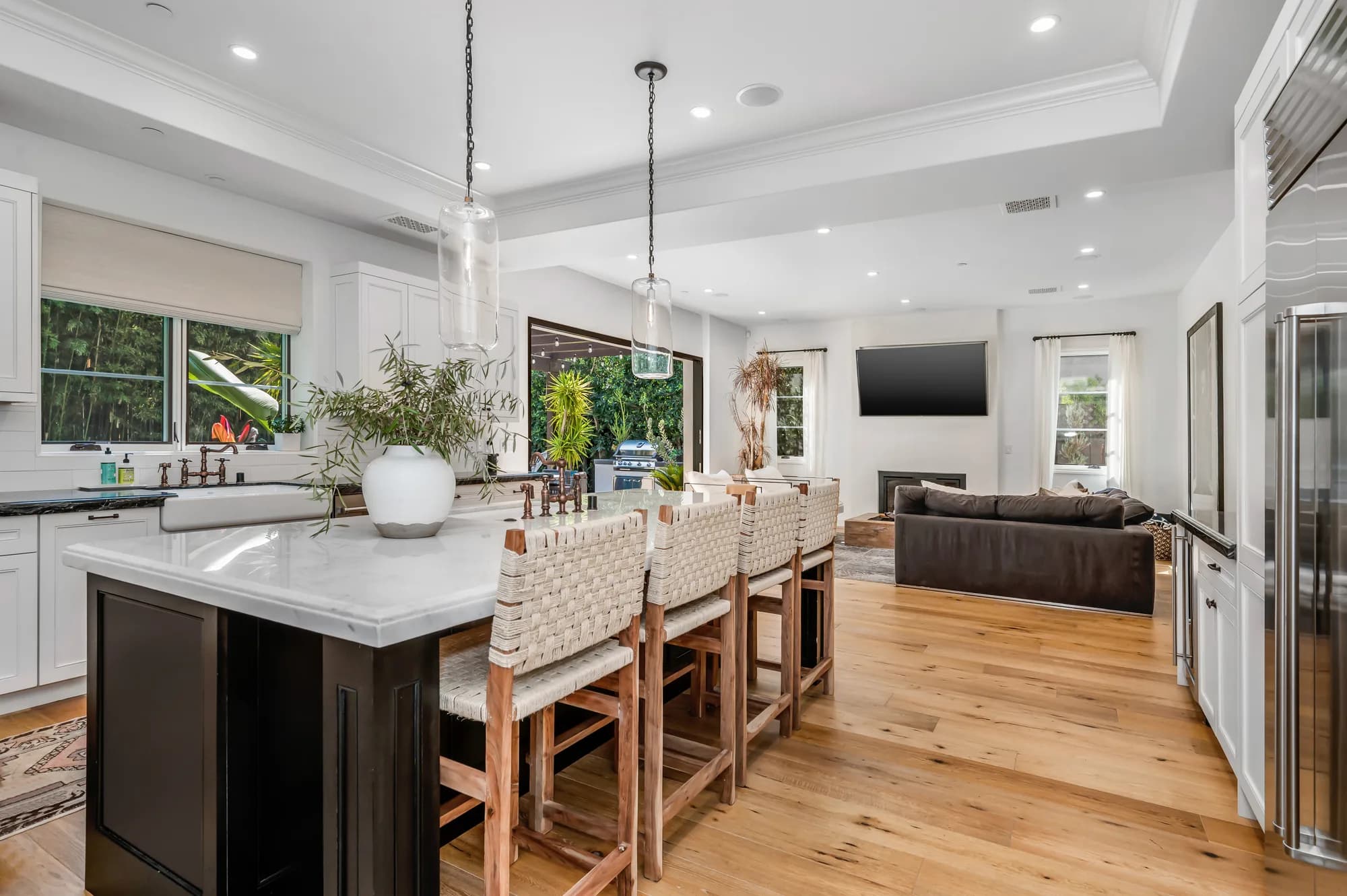 Open kitchen with a dark island, woven stools, white cabinets, and oak flooring